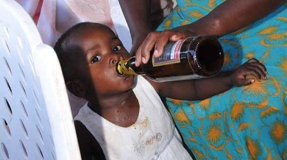 A Ugandan mother was pictured giving her daughter beer at an event. The picture is currently going viral and people are already chastising her for it.